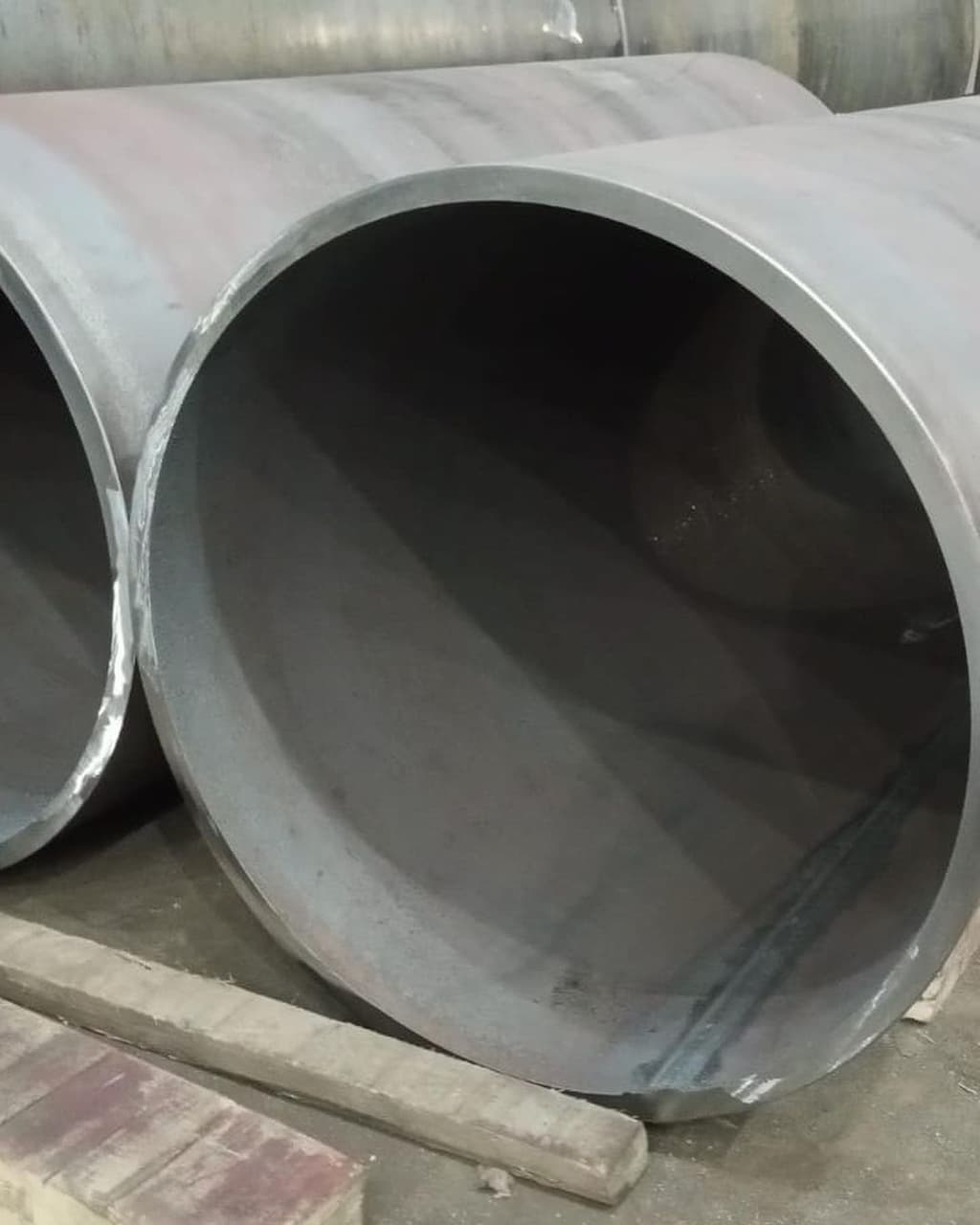 Se observan varios tubos galvanizados de gran diámetro, colocados en posición horizontal sobre una superficie de concreto. Estos tubos tienen un acabado metálico y están parcialmente cubiertos por un material gris. También hay una base de ladrillos visible en la parte inferior de la imagen.