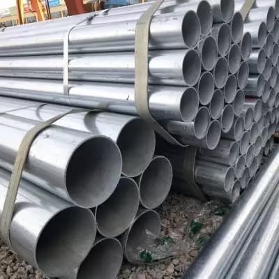 Se observan varios tubos galvanizados apilados y atados entre sí, con algunos espacios visibles entre ellos. Están colocados sobre una superficie de grava.